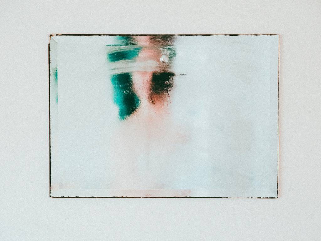 Image of a rectangle mirror on a wall with a blurry individual taking a self-portrait.